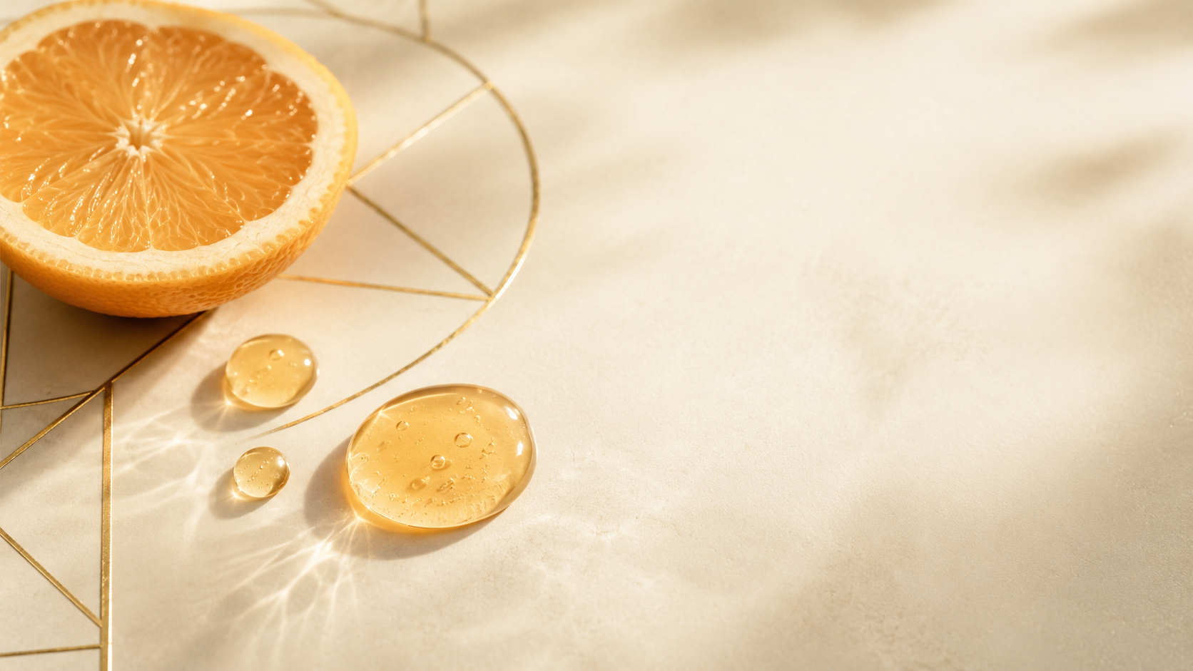 Halved citrus and amber serum droplets on a warm-ivory surface with a thin gold-line motif in soft daylight